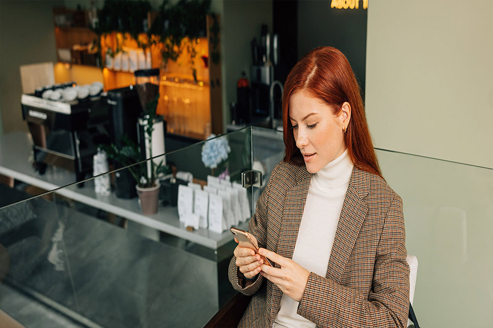 mujer en una cafeteria mirando su celular novibet